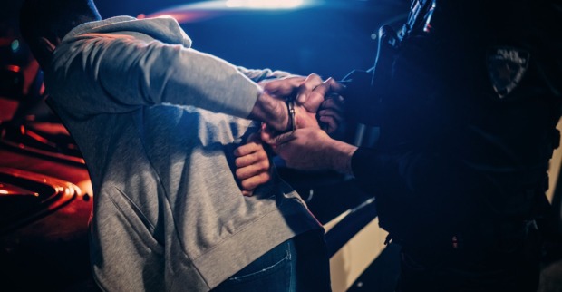 Ein Mann wird von einem Polizisten mit Handschellen festgenommen.