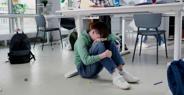 Ein Bub sitzt weinend auf dem Boden im Klassenzimmer.