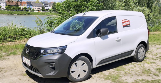 Ein weißer Nissan Townstar glänzt in der Sonne. Das Auto steht am Ufer eines Flusses, auf einem sandigen Parkplatz. Am anderes Ufer sind mehrere Häuser zu sehen.