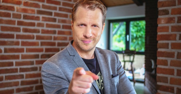 Oliver Pocher mit einem grauen Anzug. Er zeigt in die Kamera.