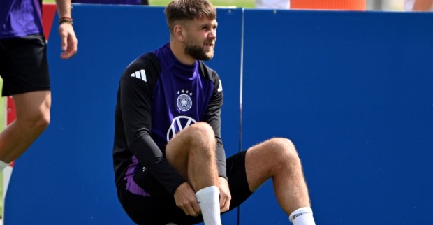 Niclas Füllkrug sitzt am Rasen auf einem Fußball.