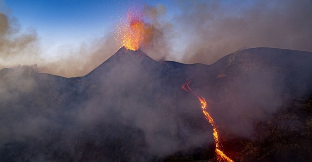 Der Ätna bei Dämmerung spuckt Lava und Rauchwolcken, an der Seite des Vulkan fließt Lava herab