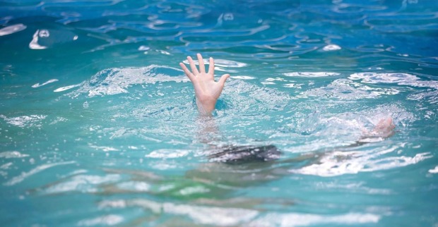 Die Hand eines Kindes schaut aus dem Wasser eines Hallenbads.