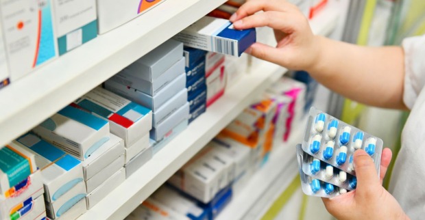 Apothekerin sortiert Medikamente im Regal einer Apotheke