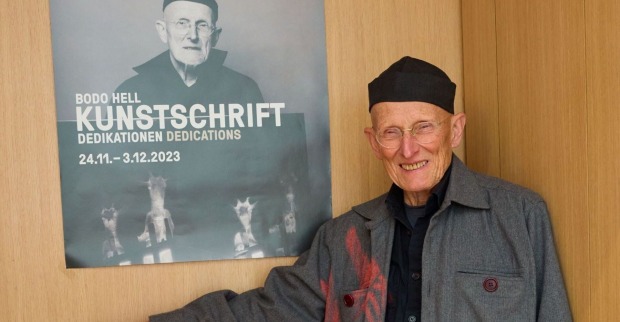 Bodo Hell vor einem Plakat, das ihn selbst zeigt.
