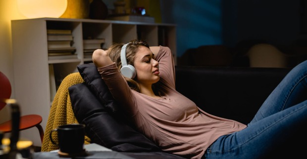 Frau liegt auf der Couch mit Kopfhörern | Credit: iStock.com/Dejan_Dundjerski