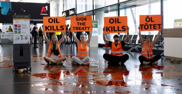 Vier Klimaaktivisten mit Protestschildern und verschütteter Farbe.