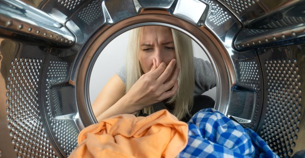 Frau nimmt stinkende Wäsche aus der Waschmaschine | Credit: iStock.com/Olga Ihnatsyeva