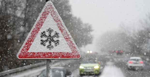 Winterliche Verhältnisse auf einer Straße und ein Schneefall-Warnschild.