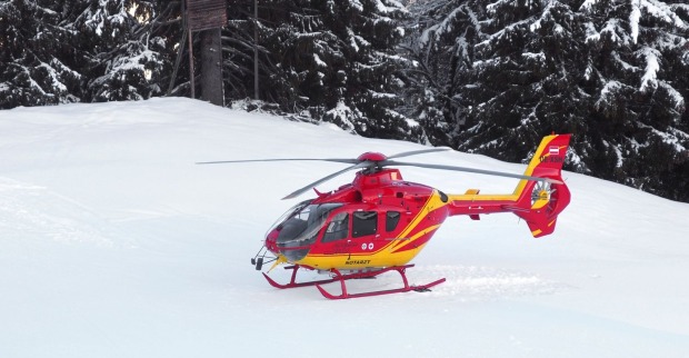 Rot-gelber Rettungshubschrauber auf einer Skipiste.