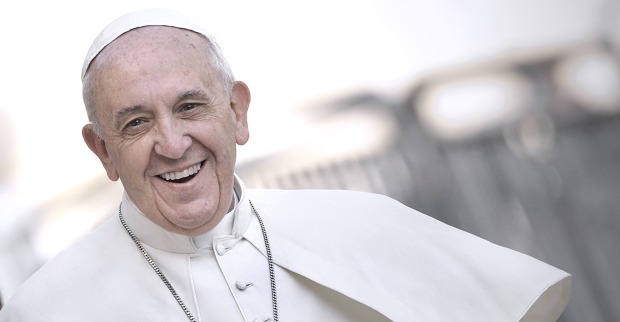 Porträt von Papst Franziskus aus dem Jahr 2013 mit freundlichem Lächeln im weißen Ornat im Freien, leicht seitlich aufgenommen.