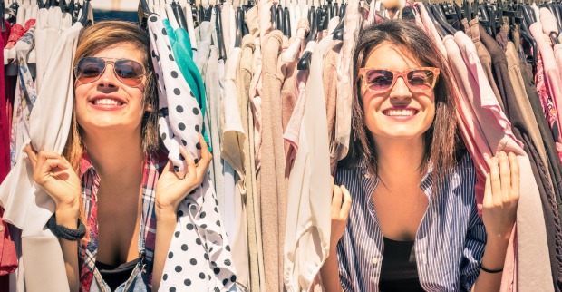 Zwei junge Frauen schauen zwischen Klamotten hervor.