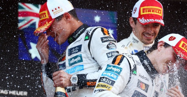 Lando Norris spritzt mit Champagner, neben ihm Oscar Piastri und Charles Leclerc auf dem Podium des Formel-1-Rennens in Monaco 2025, alle tragen Pirelli-Kappen und Rennanzüge.