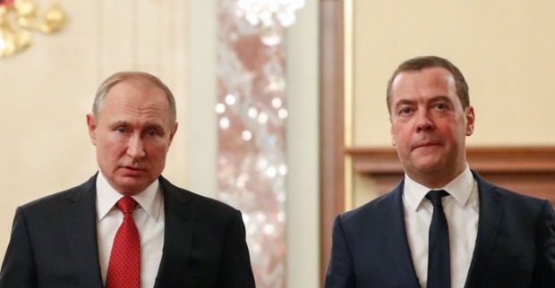 Wladimir Putin und Dmitri Medwedew in Anzug und Krawatte während eines offiziellen Termins im Kreml, ernster Gesichtsausdruck vor prunkvollem Hintergrund.