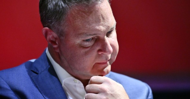 Andreas Babler in einem blauen Anzug vor rotem Hintergrund, mit nachdenklichem Gesichtsausdruck und der Hand am Kinn.