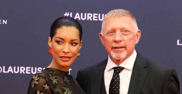 Boris Becker im schwarzen Anzug mit gepunkteter Krawatte und seine Frau Lilian de Carvalho Monteiro in einem schwarzen Kleid mit goldenen Details posieren gemeinsam auf dem roten Teppich