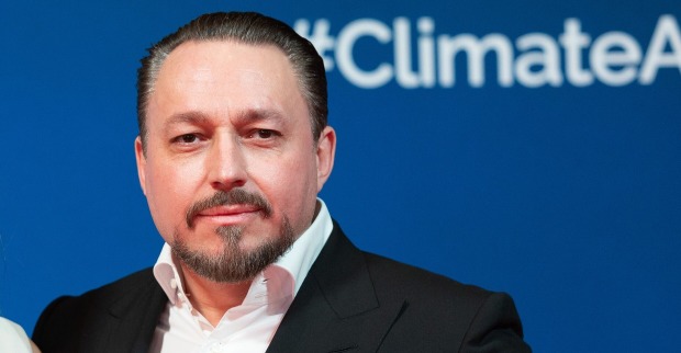 Porträt von Klemens Hallmann vor blauem Hintergrund mit „#ClimateAction“-Schriftzug, im dunklen Anzug und weißem Hemd.