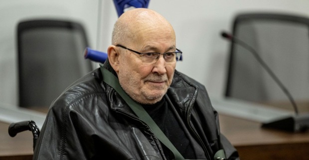 Horst Mahler sitzt im Rollstuhl, trägt eine schwarze Lederjacke und blickt ernst. Aufnahme aus einem Gerichtssaal im Jahr 2022.