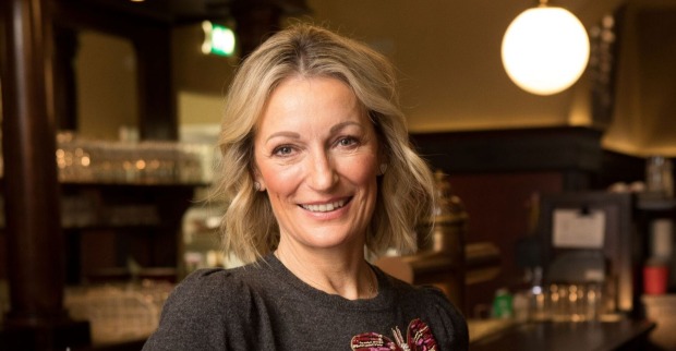 Monika Gruber lächelt in die Kamera, während sie in einer Bar steht.