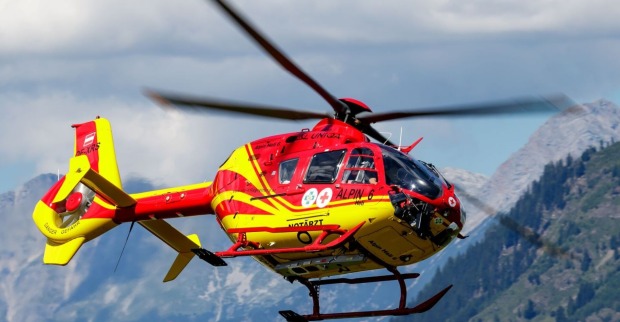 rot-gelber Notarzt Hubschrauber der Bergrettung in der Luft, Berge im Hintergrund