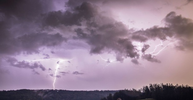 Gewitterfront mit dunklen Wolken und Blitzen über bewaldeter Landschaft