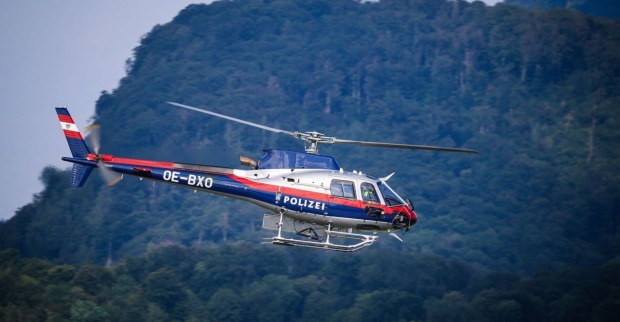 Österreichischer Polizeihubschrauber fliegt vor bewaldetem Berghang bei einer Suchaktion in Tirol.