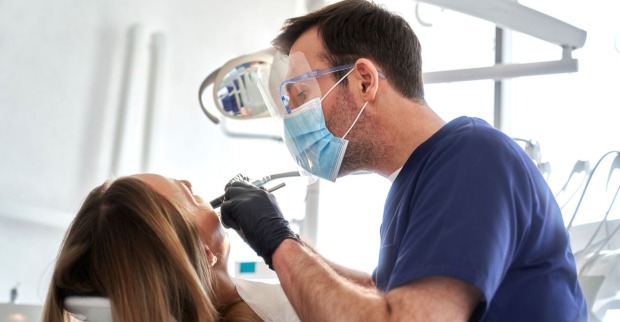 Zahnarztpraxis mit Arzt in blauer Kleidung und Patientin, die behandelt wird