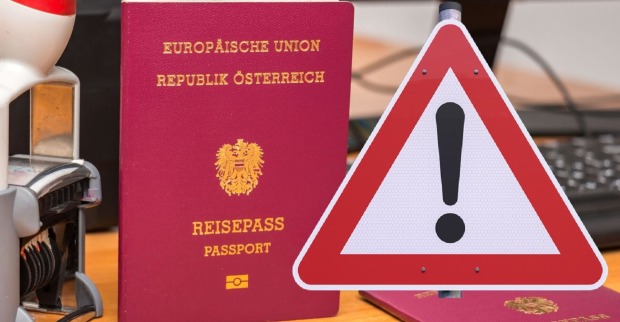 Zwei österreichische Reisepässe auf einem Schreibtisch neben einem Stempelgerät und einer Computertastatur, ein großes Warnschild.