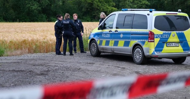 Mehrere Polizistinnen und Polizisten stehen neben einem Einsatzfahrzeug vor einem abgeernteten Feld, eine rot-weiße Absperrung ist im Vordergrund zu sehen.