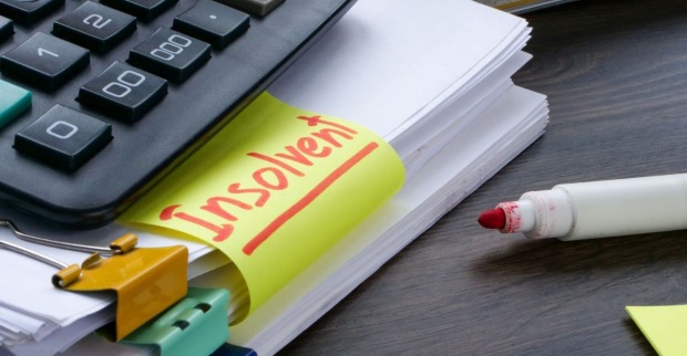 Bürotisch auf dem ein Stapel Papier mit einem Rotstift und ein Taschenrechner, auf einem Post-it steht das Wort insolvent geschrieben