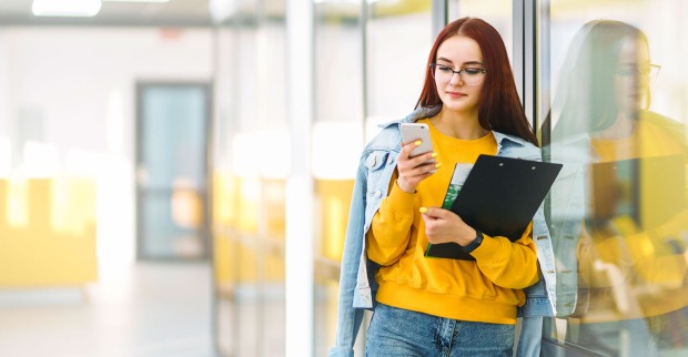 Junge Frau lehnt mit ihren Unterlagen in der Hand gegen eine Glastür | Credit: Adobe Stock