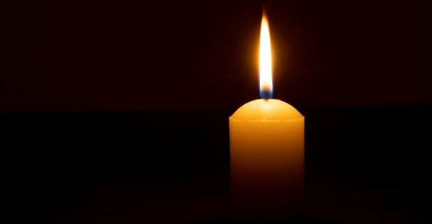 Einzelne brennende Kerzenflamme oder Licht, das auf einer großen weißen Kerze auf schwarzem oder dunklem Hintergrund auf dem Tisch in der Kirche für Weihnachten, Beerdigung oder Gedenkfeier mit Kopierraum leuchtet.