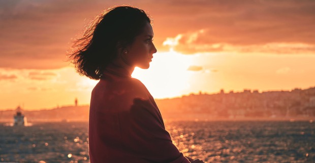 Frau steht im Sonnenuntergang | Credit: iStock.com/RomaBlack