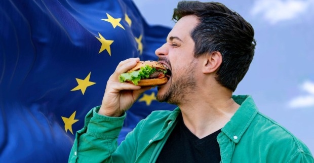 Mann mit grünem Hemd isst einen Burger vor einer wehenden EU-Flagge; Symbolbild zur EU-Entscheidung über das Verbot von Bezeichnungen wie „Veggie-Burger“ oder „Soja-Schnitzel“.