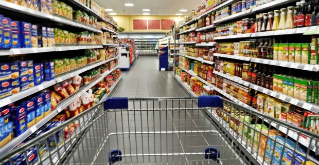 Einkaufswagen in einem Supermarkt, auf den Regalen stehen Lebensmittel und andere Waren