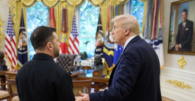 Donald Trump und Wolodymyr Selenskyj stehen im Oval Office des Weißen Hauses und sprechen miteinander, umgeben von US-Flaggen und goldenen Vorhängen.