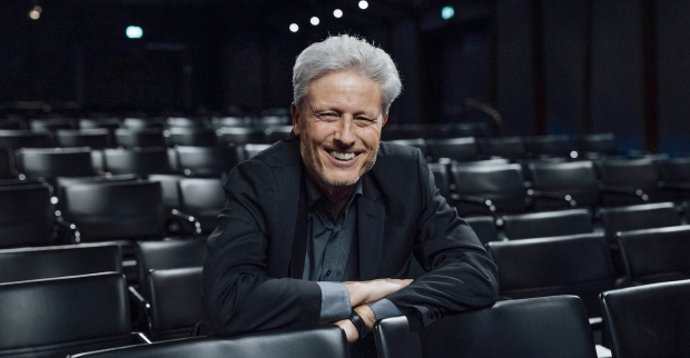 Florian Scheuba in dunklem Hemd und schwarzen Anzug im Zuschauerraum eines Theaters