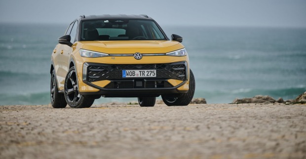 Ein gelber VW T-Roc parkt vor dem Meer, das kaum Wellen aufweist. Der Untergrund auf dem das Auto steht besteht aus Stein.