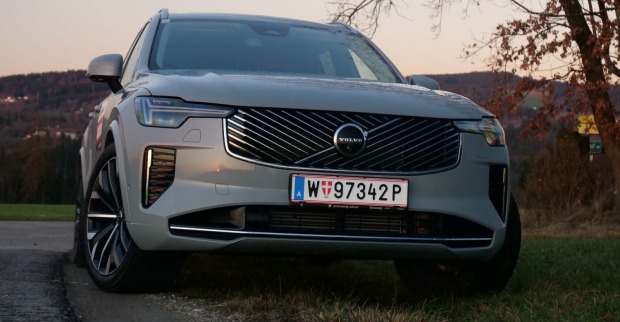 Eine silberner Volvo XC90 von vorne. Das Auto ist in der Abenddämmerung zu sehen, im Hintergrund ist eine Hügellandschaft zu erkennen.