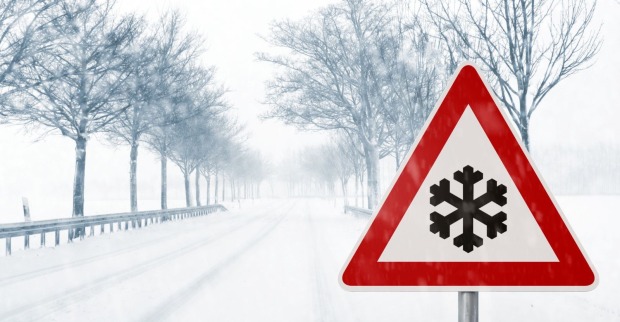 Warnschild mit Symbol für starken Schneefall auf einer verschneiten Landstraße