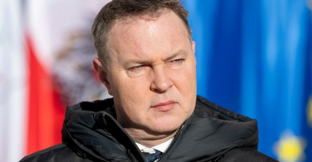 Andreas Babler blickt ernst zur Seite, im Hintergrund sind die Flaggen Österreichs und der Europäischen Union zu sehen.