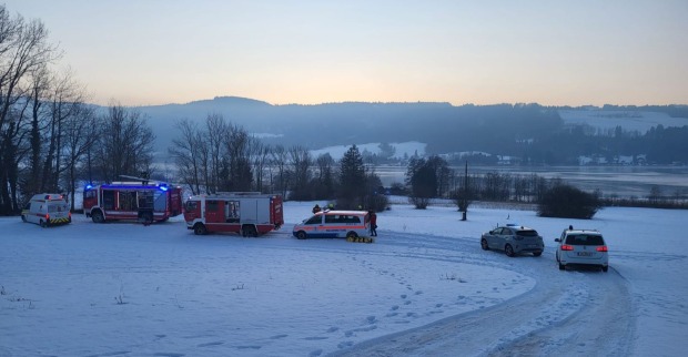 Mehrere Einsatzfahrzeuge von Feuerwehr, Wasserrettung und Polizei stehen auf einer verschneiten Wiese am Irrsee in Oberösterreich während eines Rettungseinsatzes bei winterlicher Abenddämmerung.
