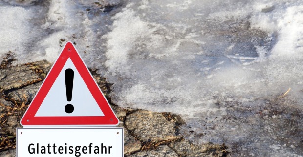 Warnschild für Glatteisgefahr und Eis im Hintergrund.