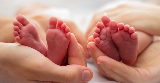 Zwillinge: Mutter und des Vaters Hände wiegt zwei Babys Füße auf einem blassen Hintergrund