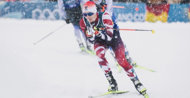 Ein österreichischer Nordischer Kombinierer in rot-weißem Rennanzug läuft bei starkem Schneefall in der Loipe während des olympischen Teamsprints in Val di Fiemme.