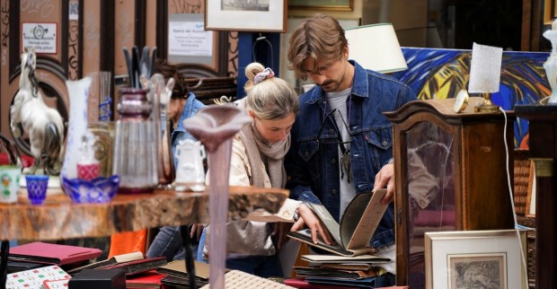 Besucher stöbern beim Flohmarkt Neubaugasse in Wien durch Vintage-Bücher, Bilderrahmen und Antiquitäten an einem Marktstand