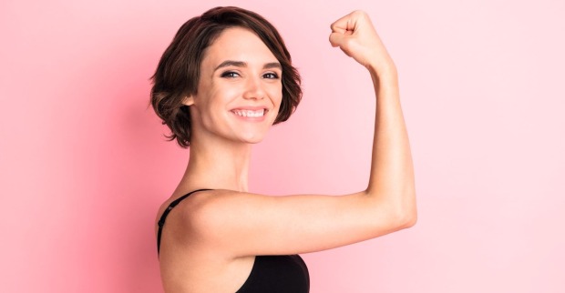 Lächelnde Frau zeigt Muskelkraft mit angewinkeltem Arm – Symbol für Energie, Fitness und die Wirkung von Magnesium im Körper