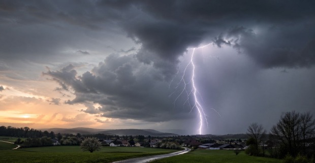 Gewitter in Österreich mit Blitz, dunklen Wolken und Regen über ländlicher Landschaft im Frühling.