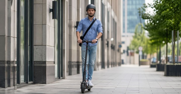 Mann fährt mit E-Scooter und trägt Helm auf Gehweg in der Stadt im Zusammenhang mit neuen StVO-Regeln für E-Scooter und E-Bikes, Helmpflicht nur für Kinder