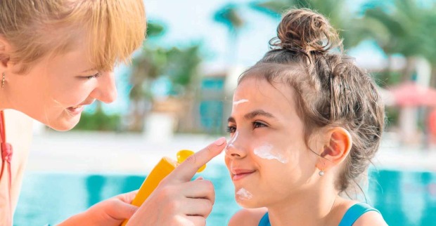 Mutter trägt ihrer Tochter am Pool Sonnencreme im Gesicht auf, um die Haut vor UV-Strahlen zu schützen.